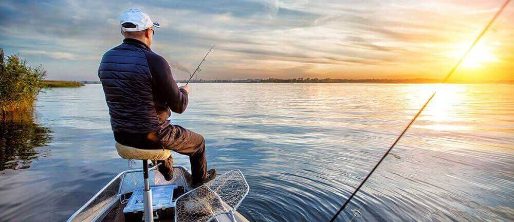 Un homme pêche de son bateau au lever du soleil