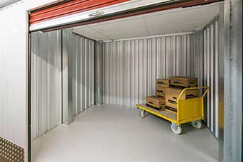 An open self storage unit with moving cart and stacks of boxes