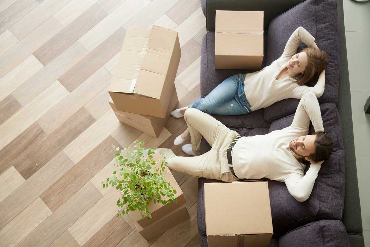 a man and woman relax on a couch with well packed boxes stacked next to them